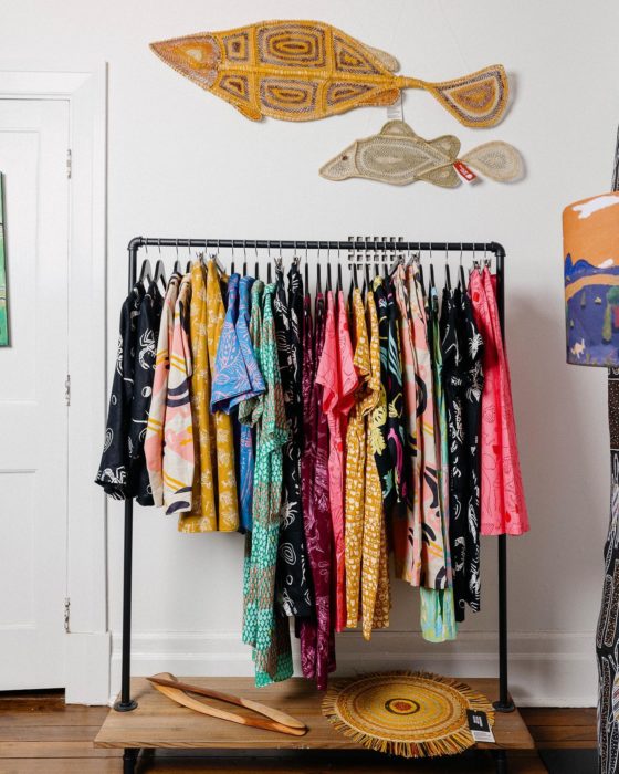 A rack of colourful clothing next to a white wall with painted fish.